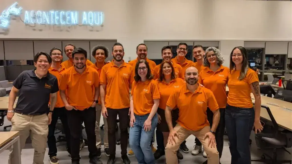 Equipe Lead Energy no escritório, com camisas polo laranja e o letreiro ACONTECEM AQUI ao fundo